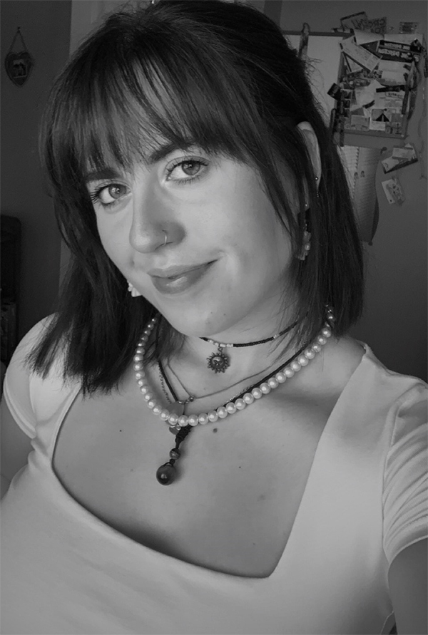 Greyscale photograph of Lucy Gerrett taken indoors, two necklaces.