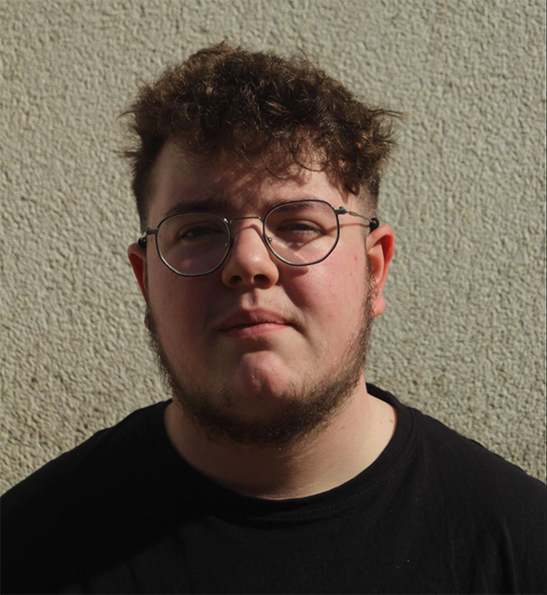 Outdoor headshot of Ryan Holloway wearing a black t shirt shot against a textured cream wall