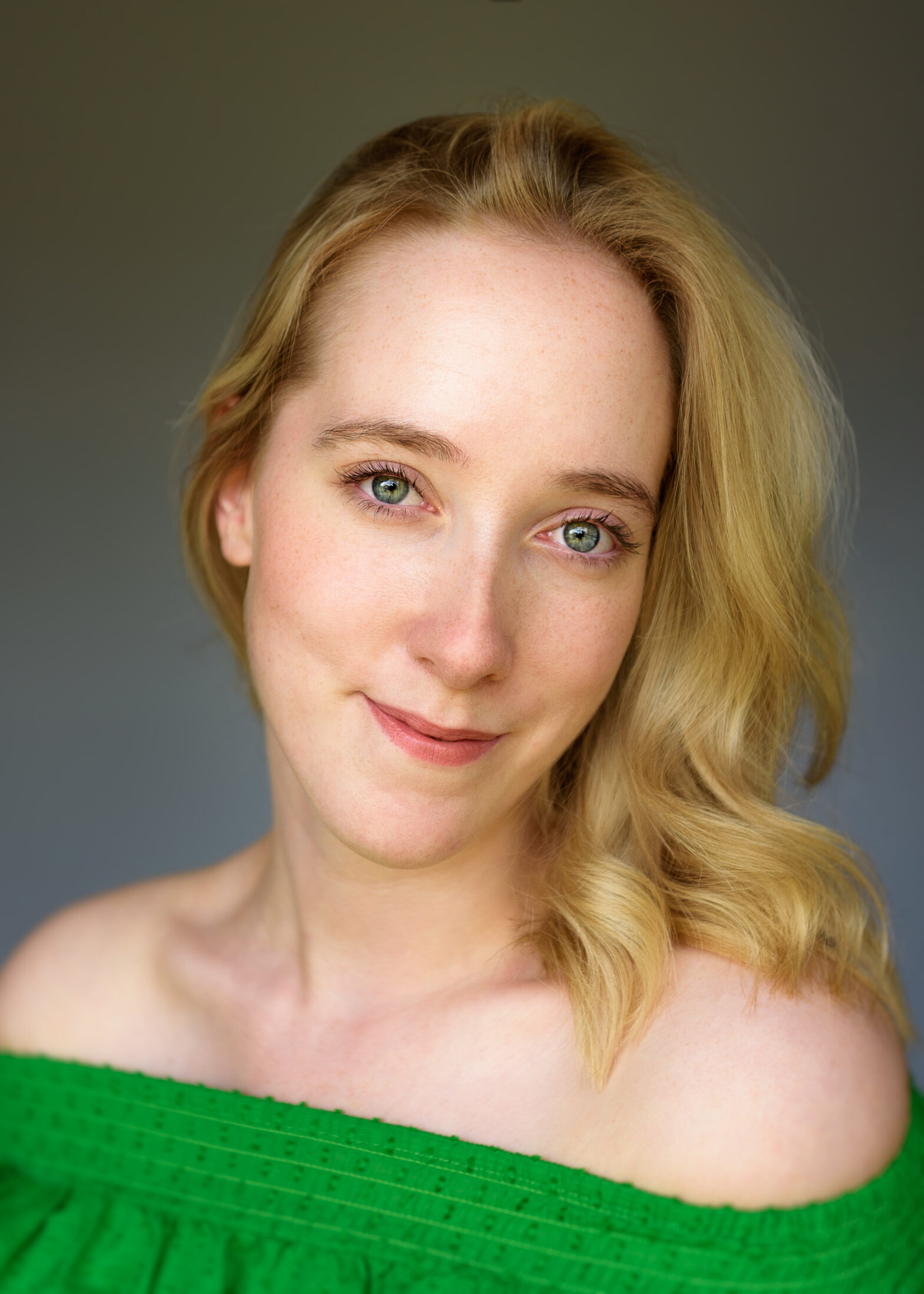 Headshot of a female artist with blonde hair curls, blue eyes and a green top.